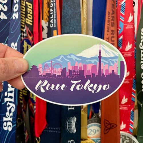 Sticker with 'Run Tokyo' design held over a collection of colorful ribbons.