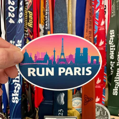 Sticker with 'Run Paris' design held in front of colorful lanyards.